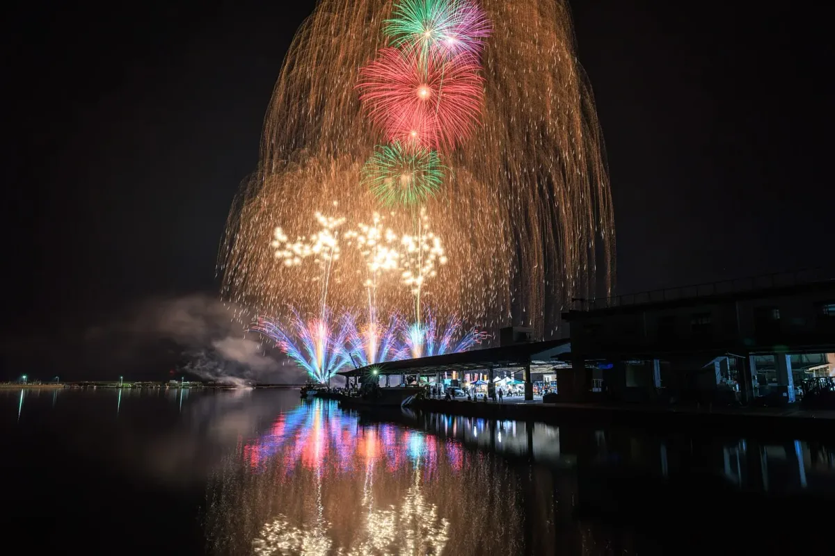 尾鷲港の建物越しに金色の大きなスターマインと赤や緑の花火が開く