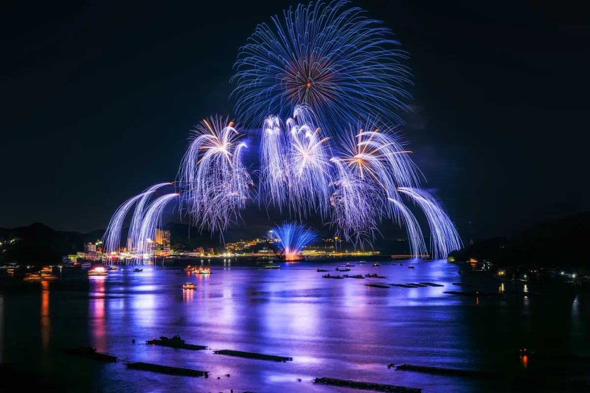 青と白の花火が鳥羽湾の夜空に咲き海面を青紫色に染める